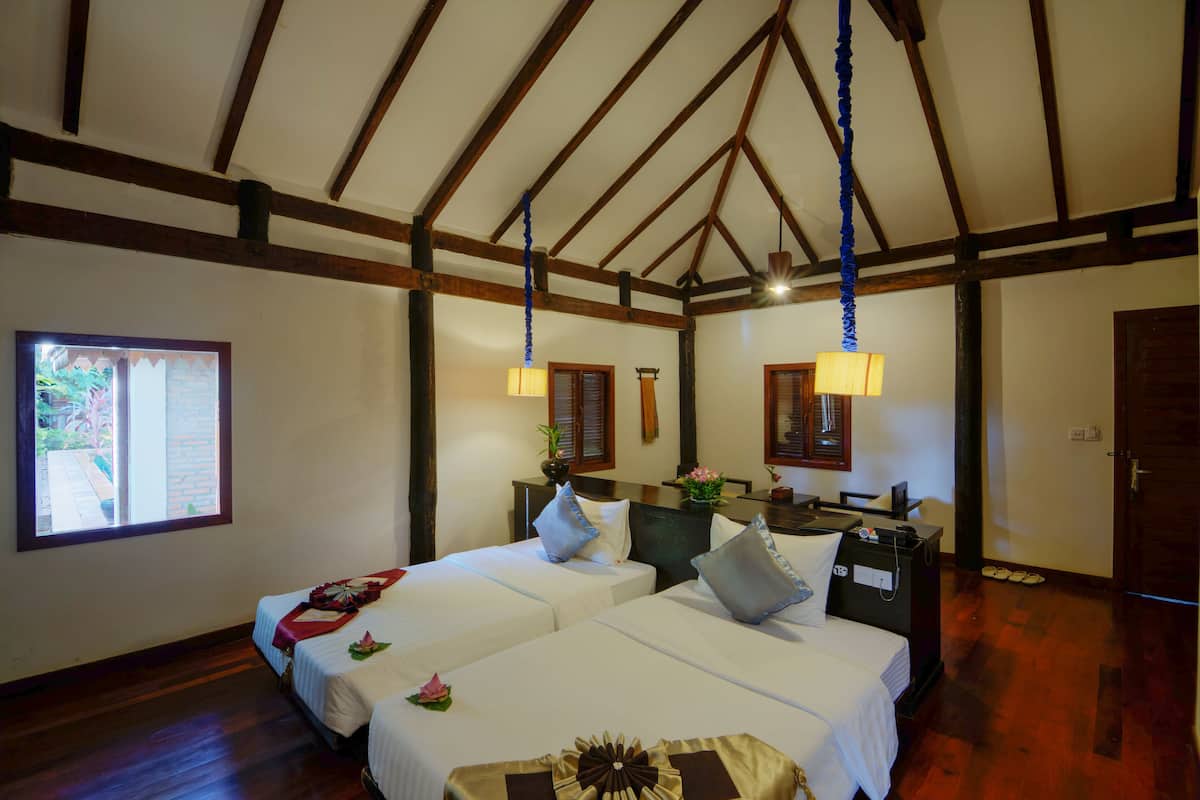 Habitación de hotel con dos camas, vigas de madera, una ventana y un escritorio con lámpara.