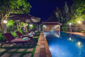 A swimming pool with lounge chairs and umbrellas, surrounded by greenery. - Bunwin Residence (Siem Reap)