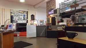 A hotel lobby with a reception desk, a piano, a whiteboard with handwritten notes, a coffee machine, and a sign for breakfast. - Hostel Colours (Milan)