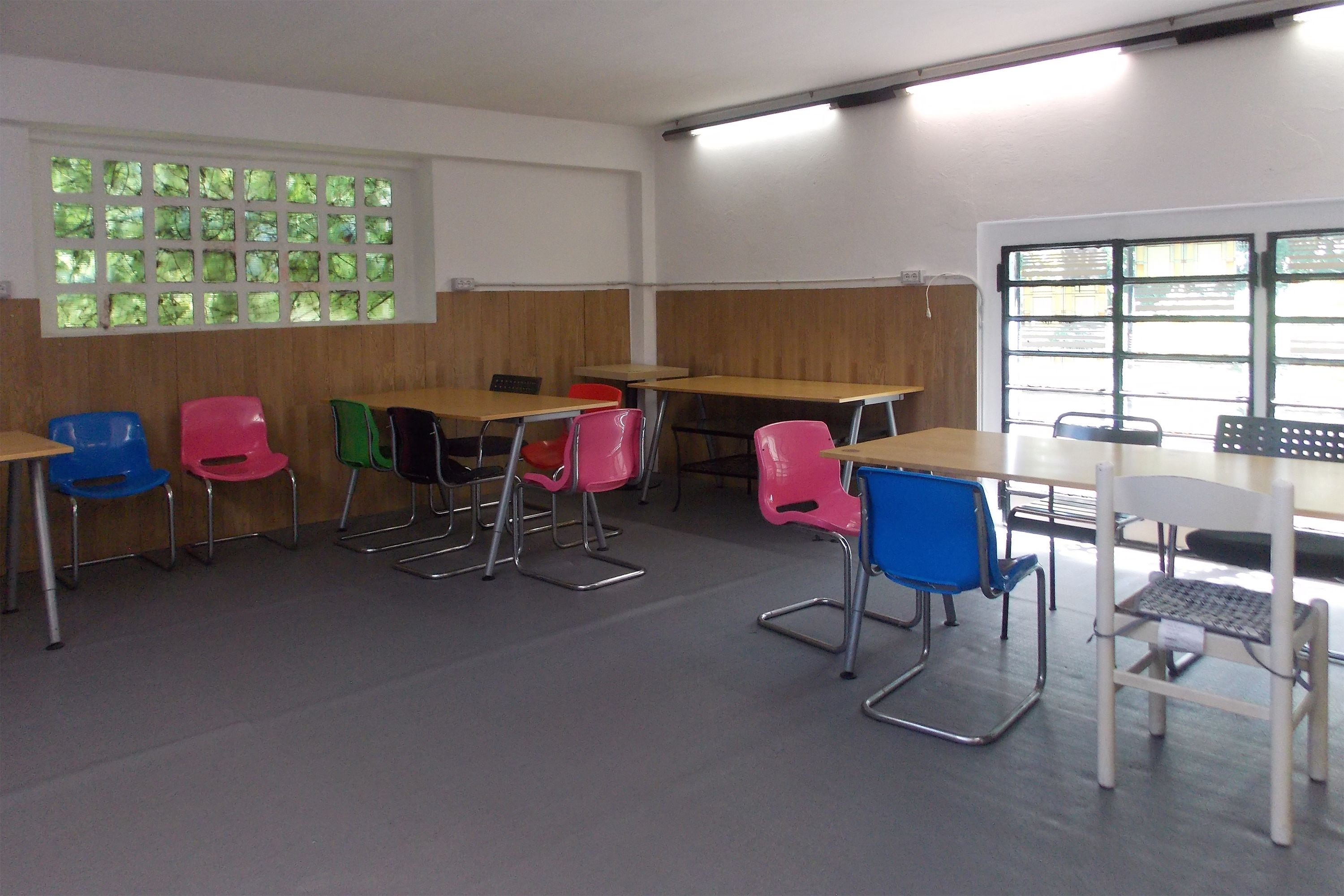 A classroom with wooden desks, colorful chairs, and a window with green-tinted glass.