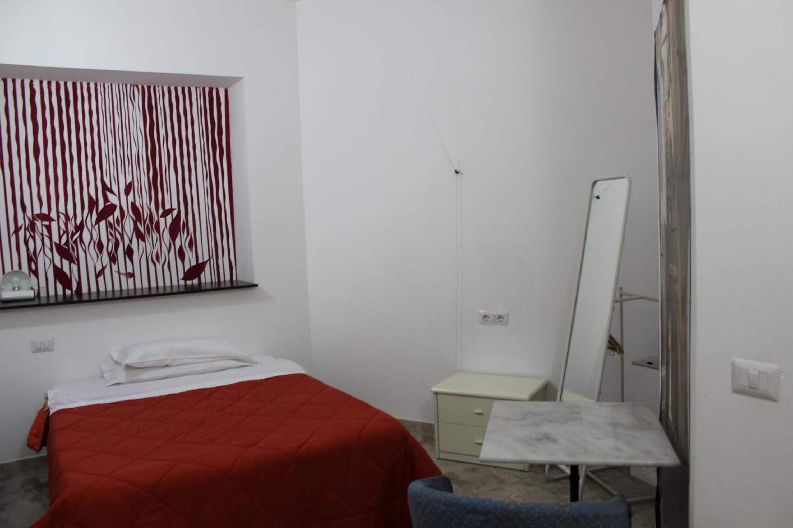 A bedroom with a bed, a desk, a chair, a mirror, and a wall art piece.