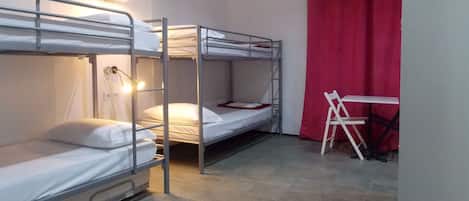 A dormitory room with bunk beds, a desk, and a red curtain.