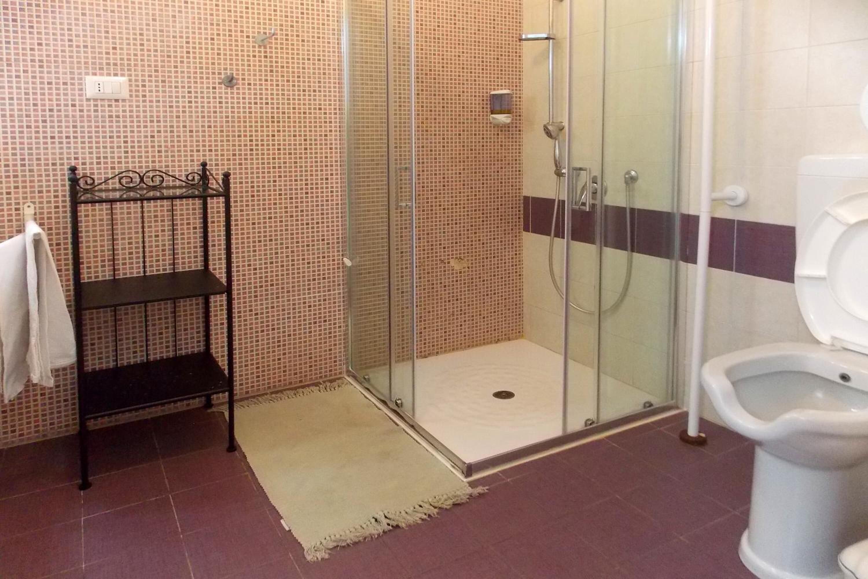 A bathroom with a glass-enclosed shower, a toilet, and a metal shelf with a towel.