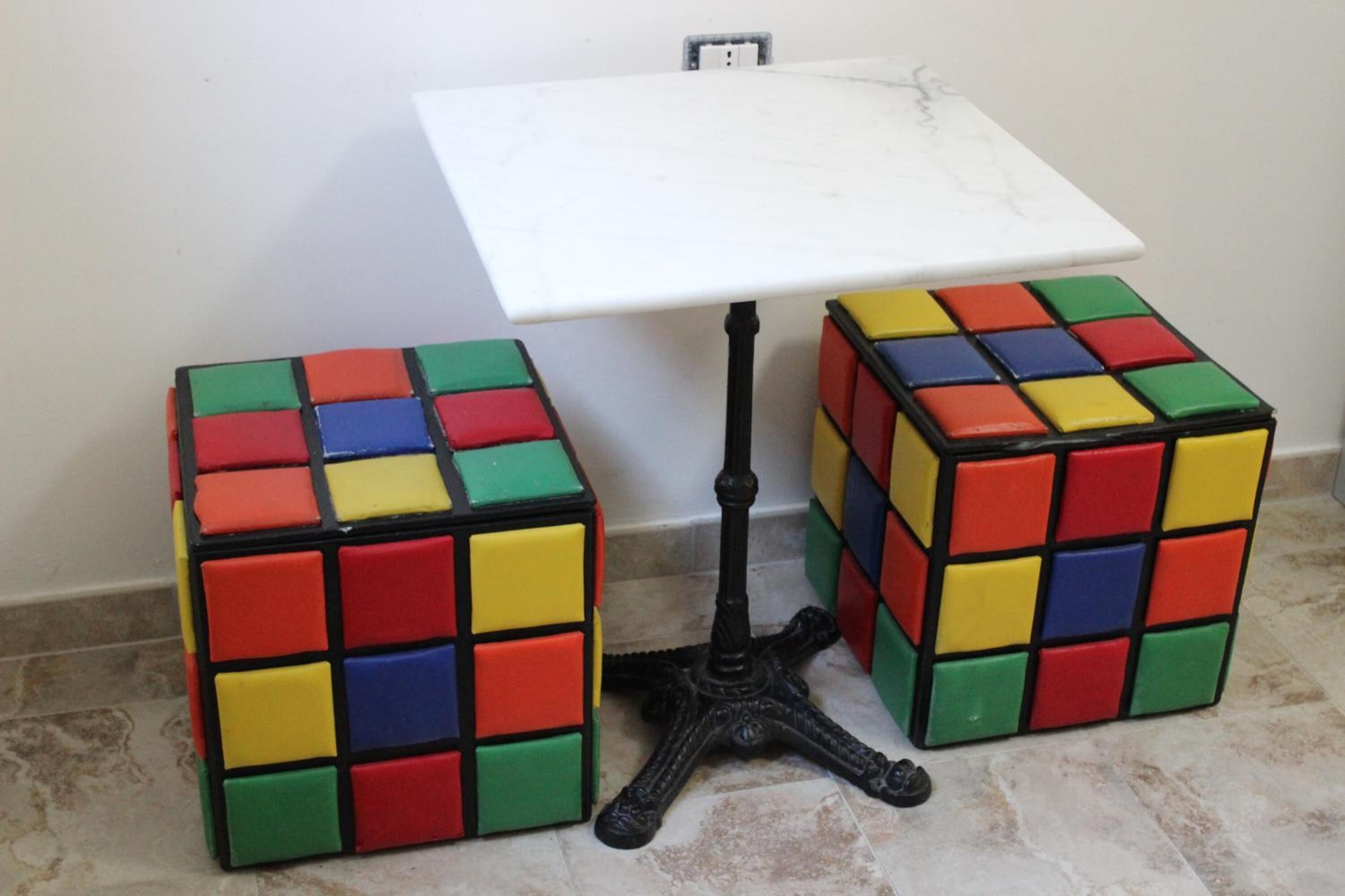 Two Rubik's cubes on a white table with a black base.