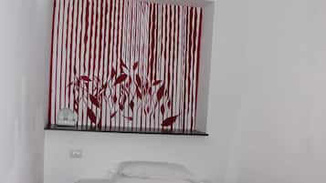 Una camera da letto con un letto, una coperta rossa, uno scaffale a parete con una sveglia e una decorazione murale a righe rosse e bianche.