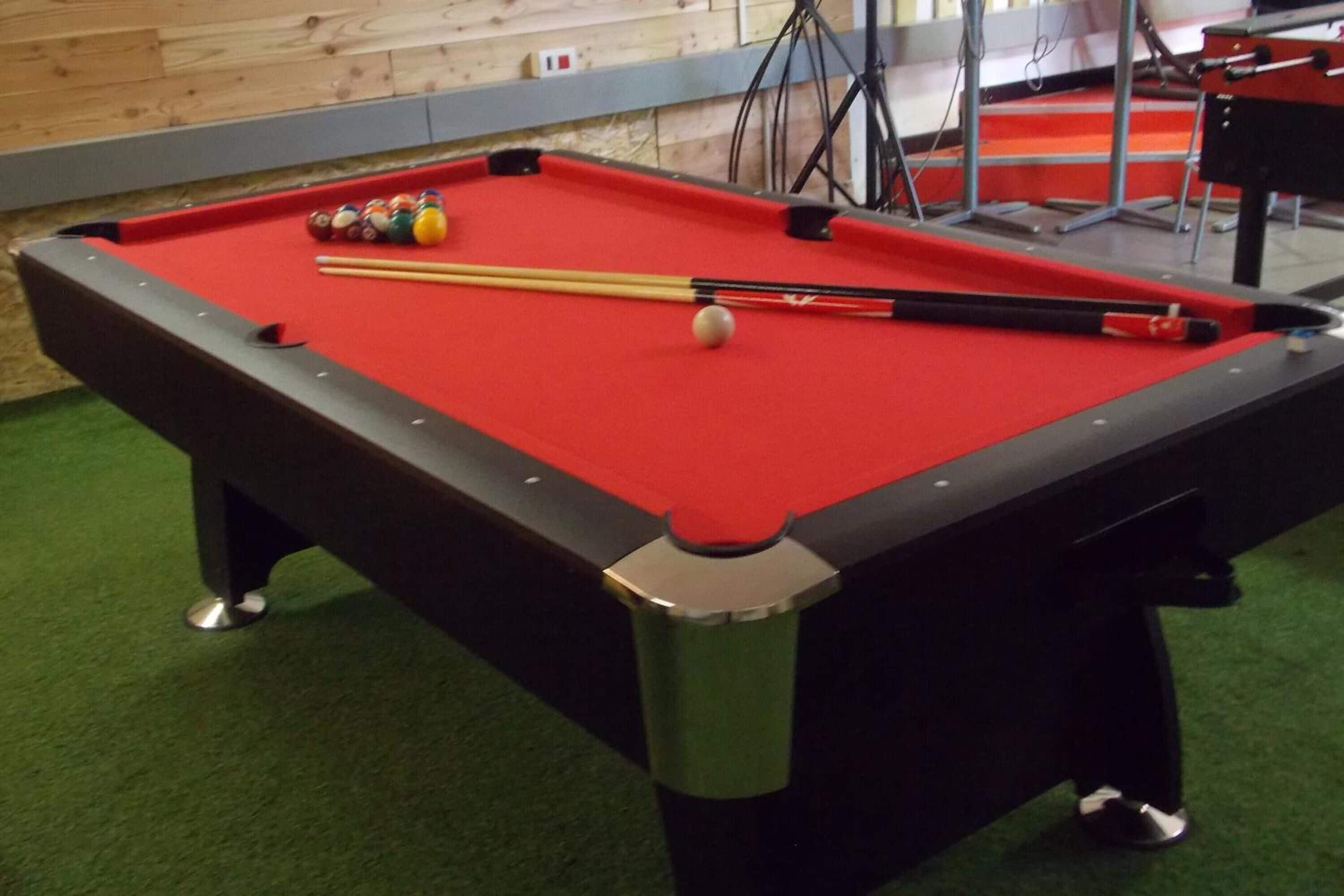 A pool table with balls and cues, a green carpet, and a wooden wall in the background.
