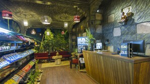Un interior acogedor con un mostrador de recepción de madera, una zona de estar con un sofá estampado en rojo y negro, y una exhibición de aperitivos.