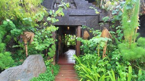 Un sendero conduce a un edificio con fachada de piedra y vegetación tropical.