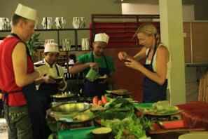 A group of people in a kitchen setting with various cooking utensils and ingredients on the counter.