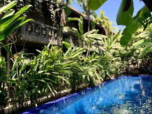 A pool surrounded by lush tropical plants and a stone building with a thatched roof. - Petit Temple Suite & Spa (Siem Reap)