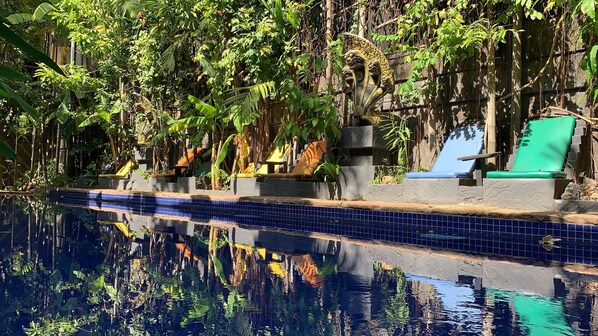 A pool with blue tiles, surrounded by lush greenery and stone structures.