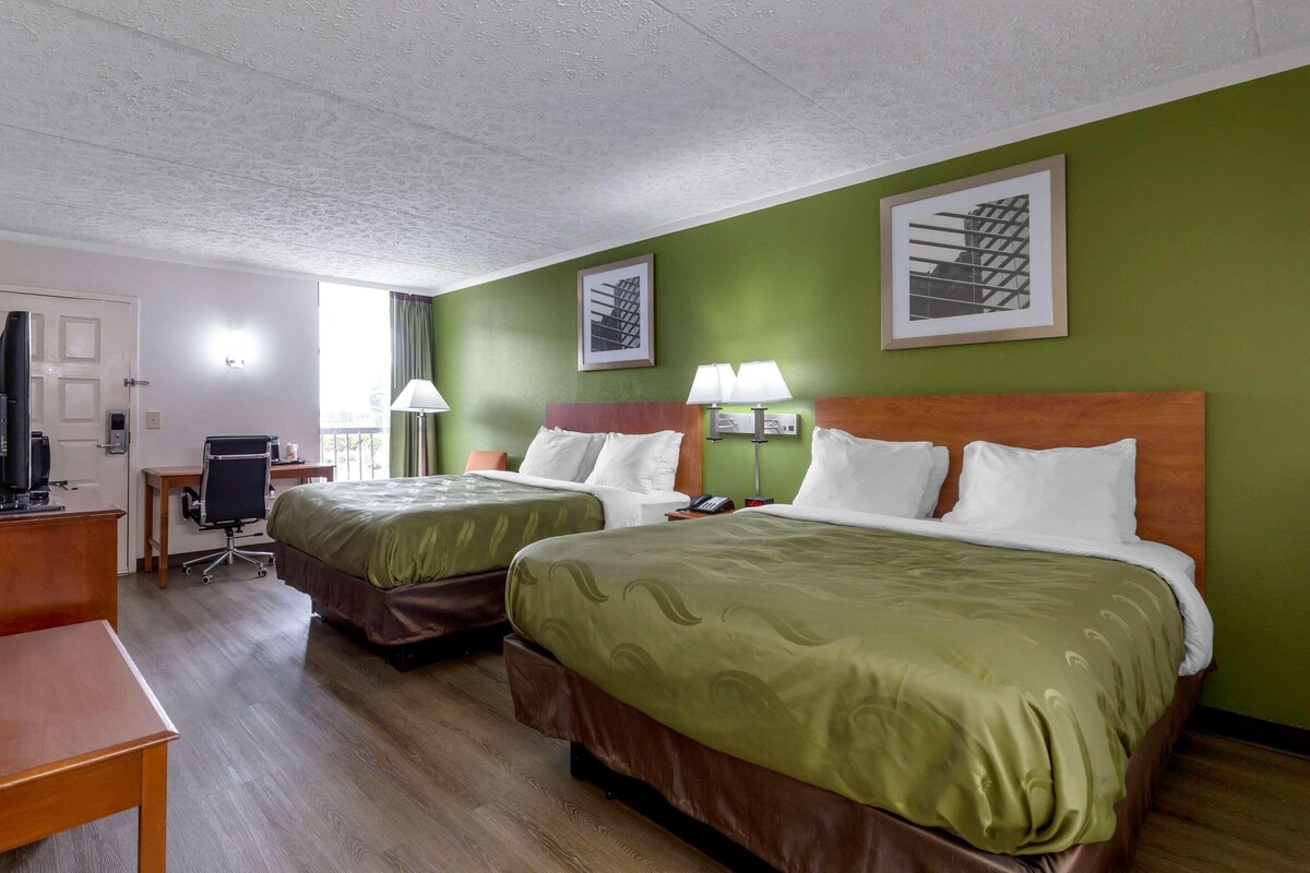 A hotel room with two beds, a desk, a chair, and a television.