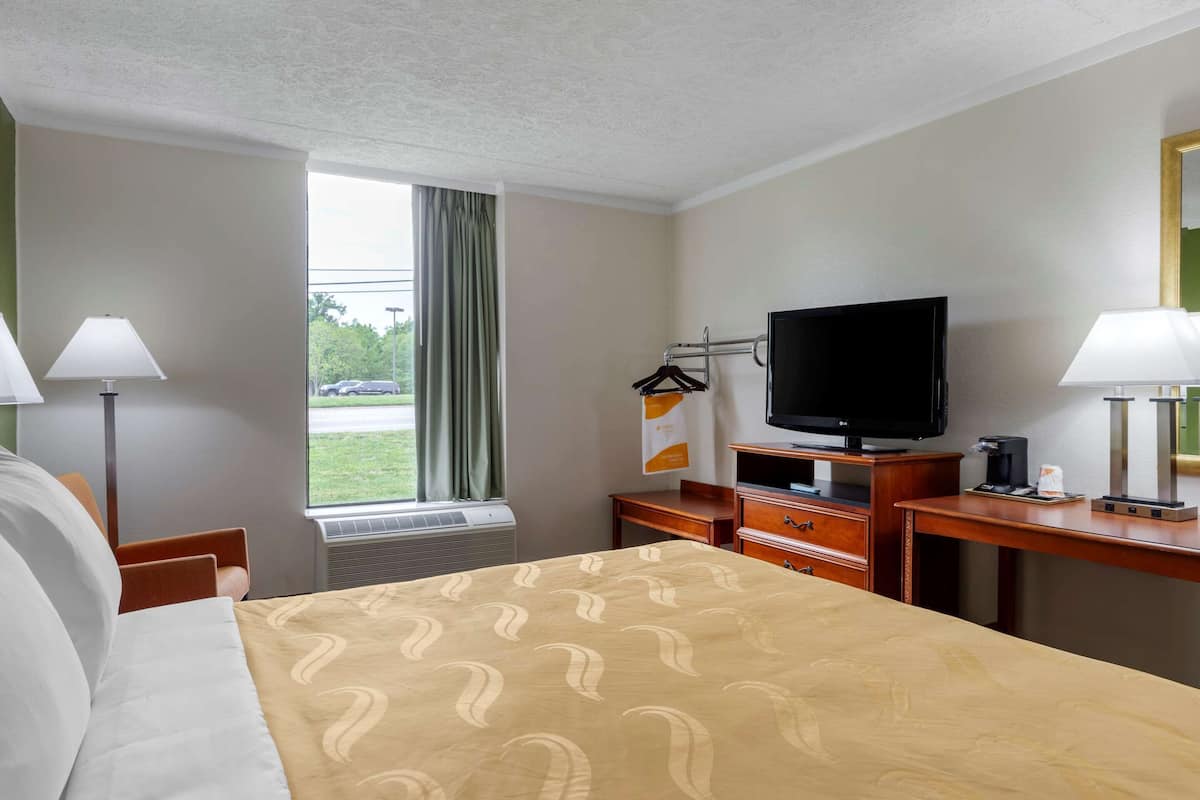 A hotel room with a bed, a desk, a television, and a window with curtains.