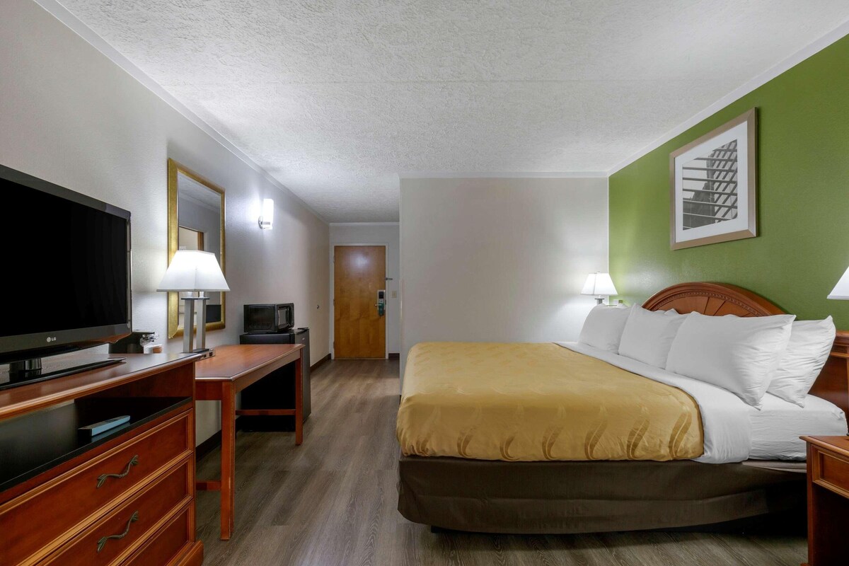 A hotel room with a bed, a desk with a TV, a lamp, and a framed picture on the wall.