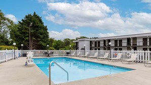 A swimming pool with a white fence, lounge chairs, and a building with multiple balconies in the background. - Quality Inn - Roxboro South (Roxboro)