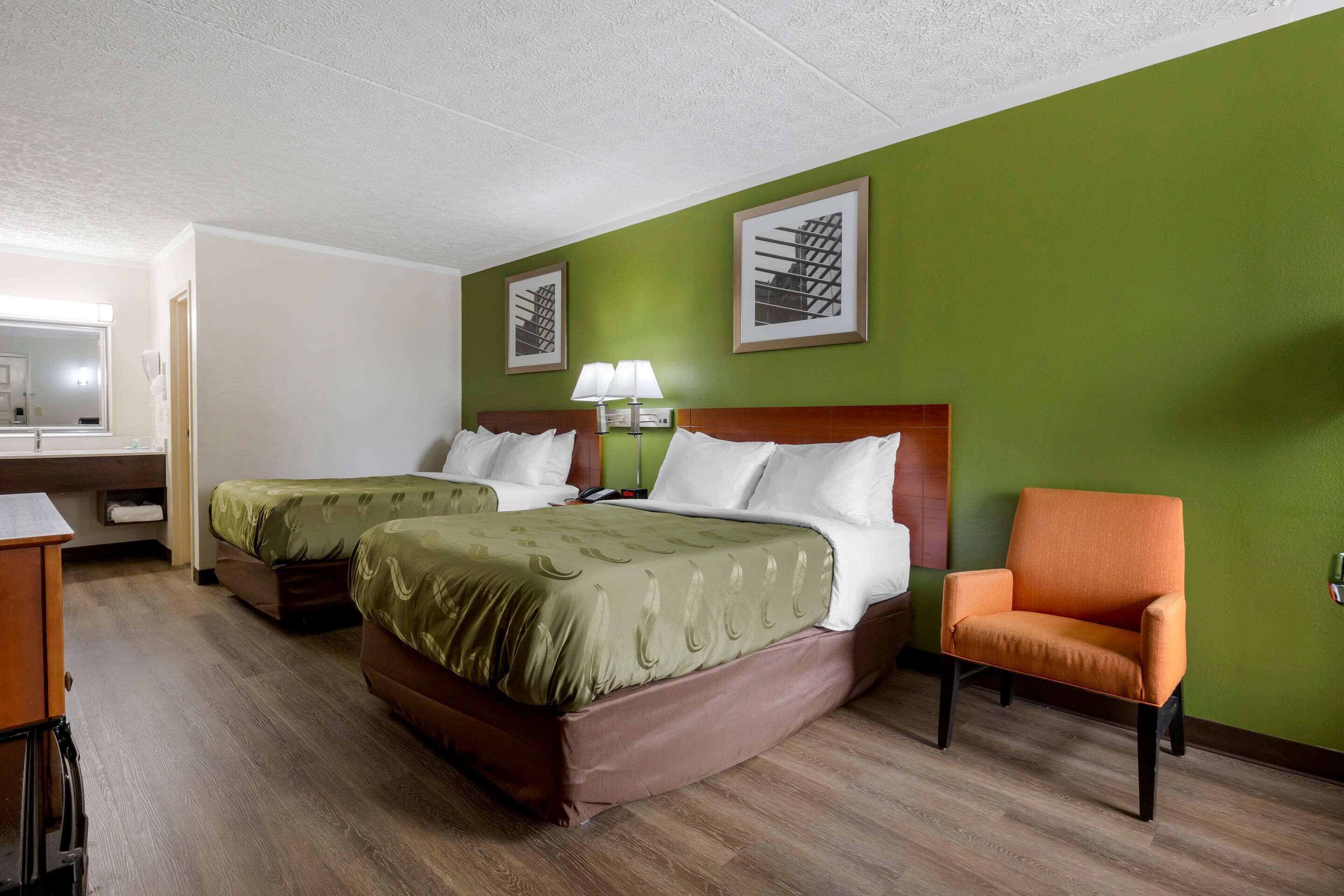 A hotel room with two beds, a desk, a chair, and green walls.