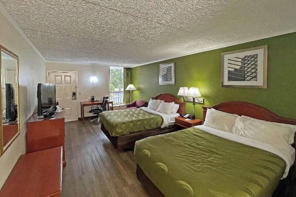 A hotel room with two beds, a desk, a chair, a TV, and a window.