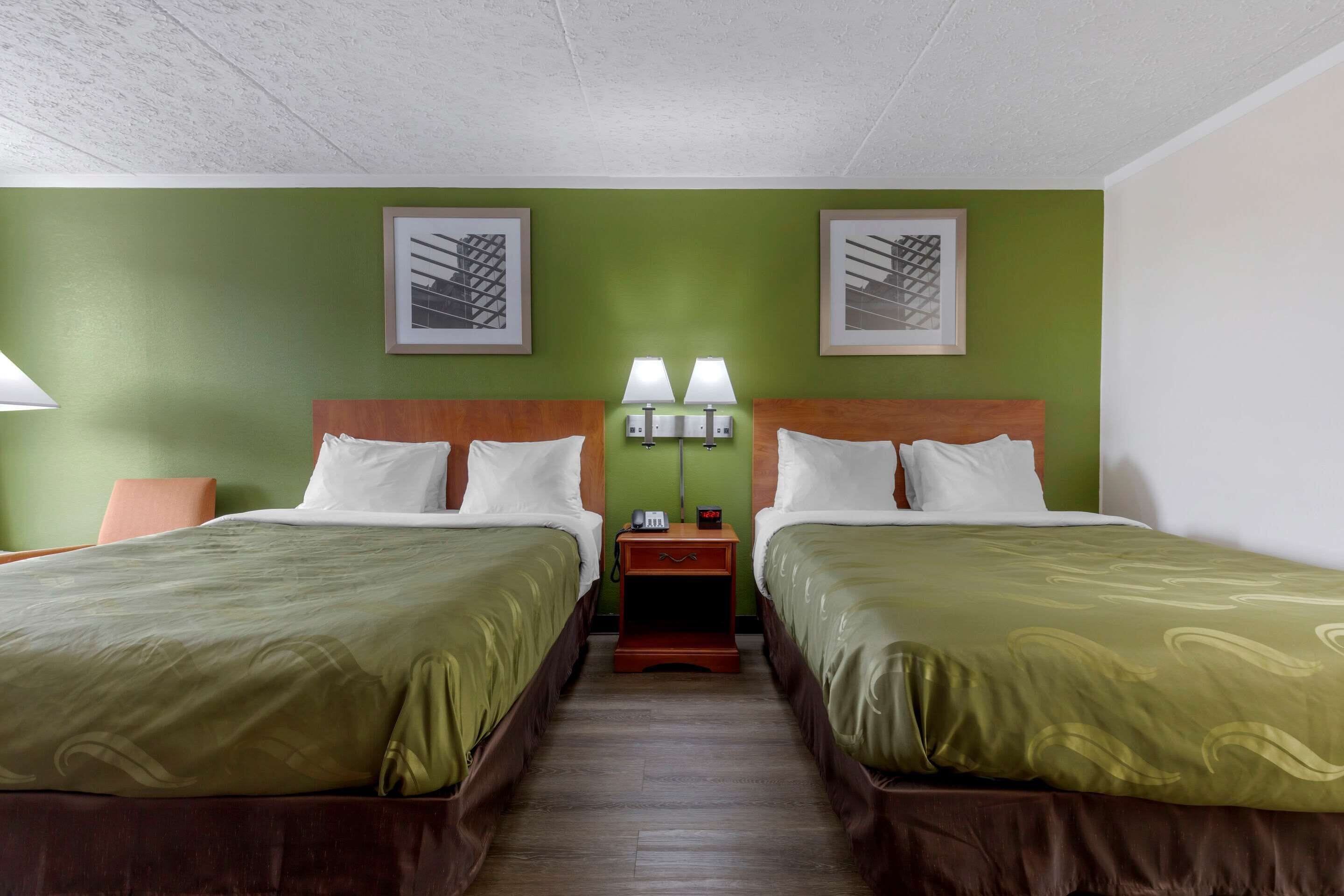 A hotel room with two beds, green walls, and artwork above the beds.