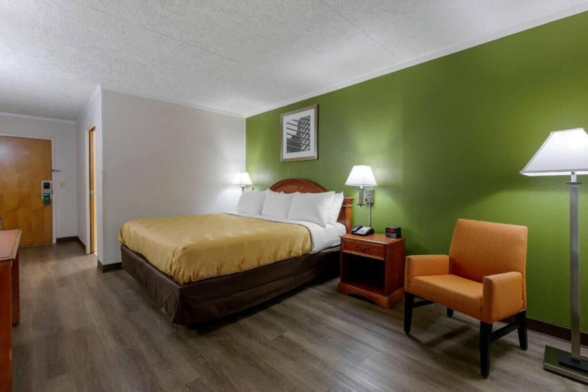 A hotel room with a bed, two bedside tables, a chair, and a green wall.