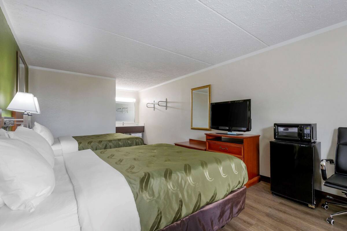A hotel room with two beds, a television, a microwave, and a desk.