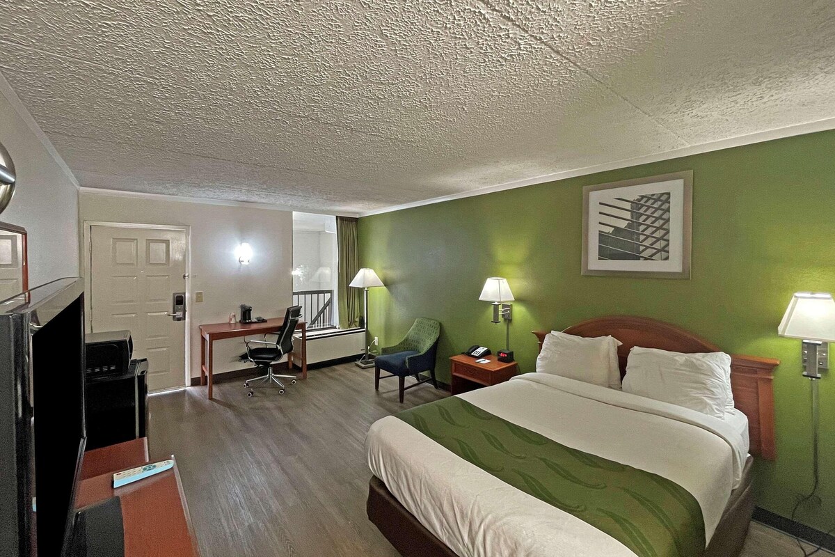 A hotel room with a bed, desk, chair, and a television.