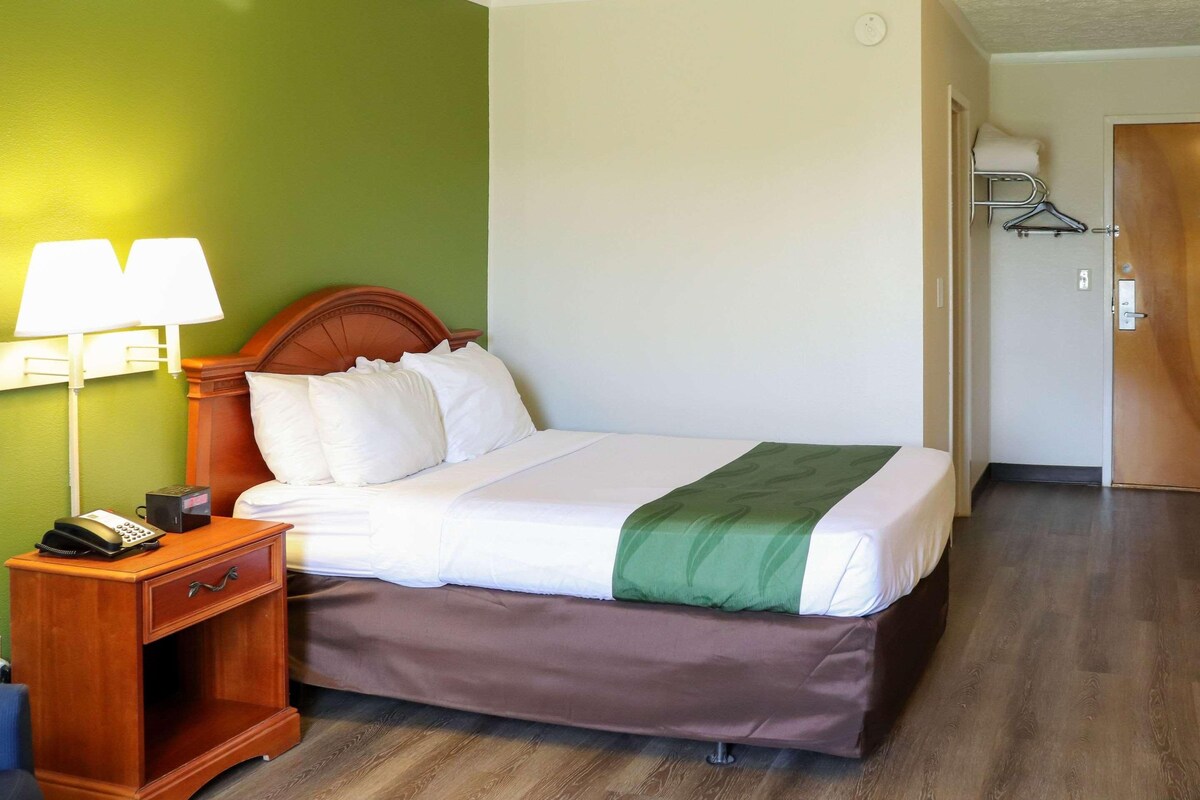 A hotel room with a bed, a nightstand with a lamp, and a coat rack.