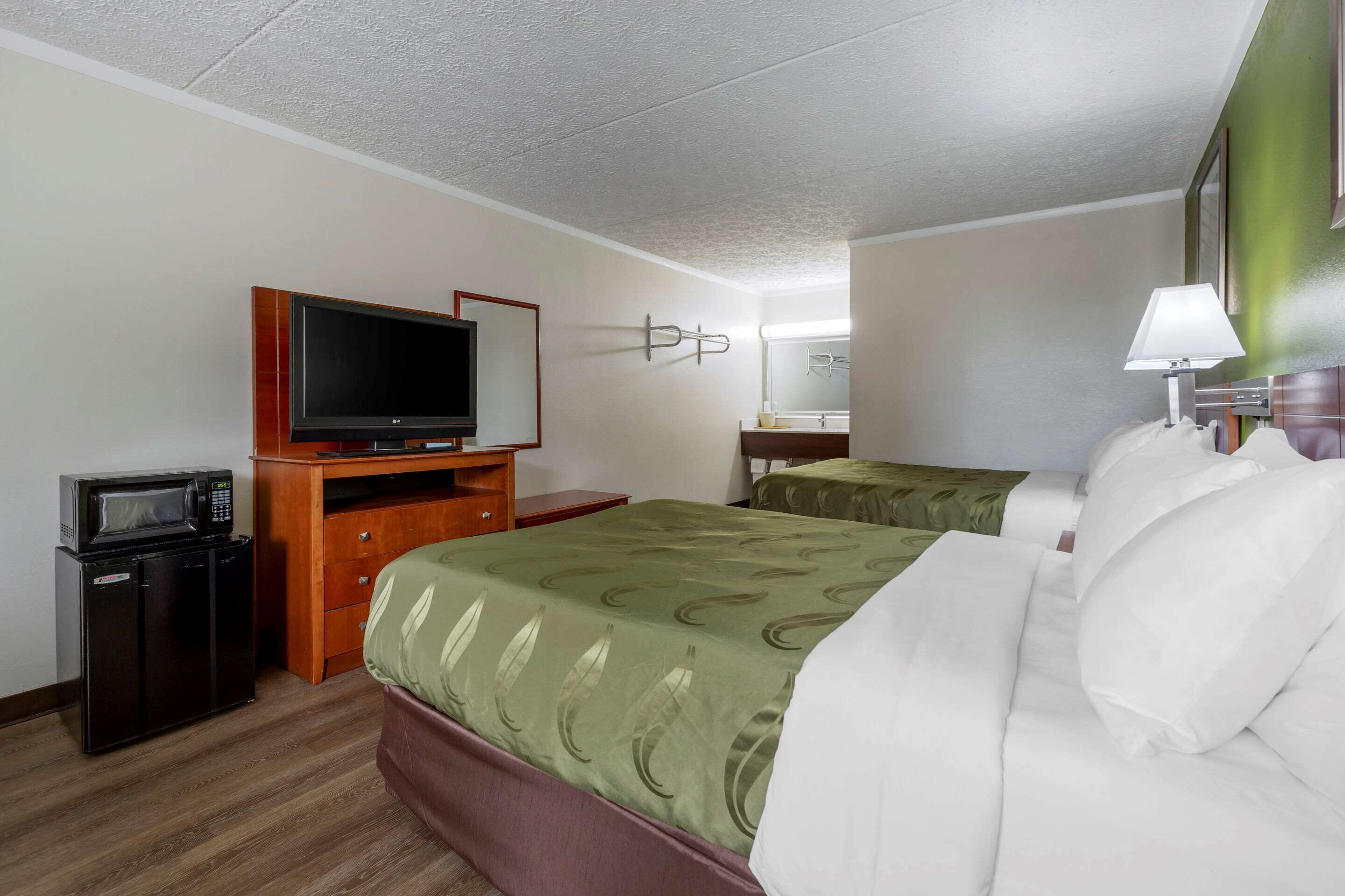 A hotel room with a single bed, a desk with a television, a microwave, and a small refrigerator.