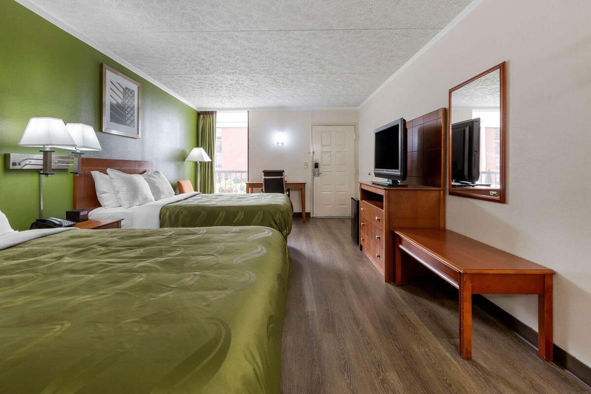 A hotel room with two beds, a TV, a desk, and a chair.
