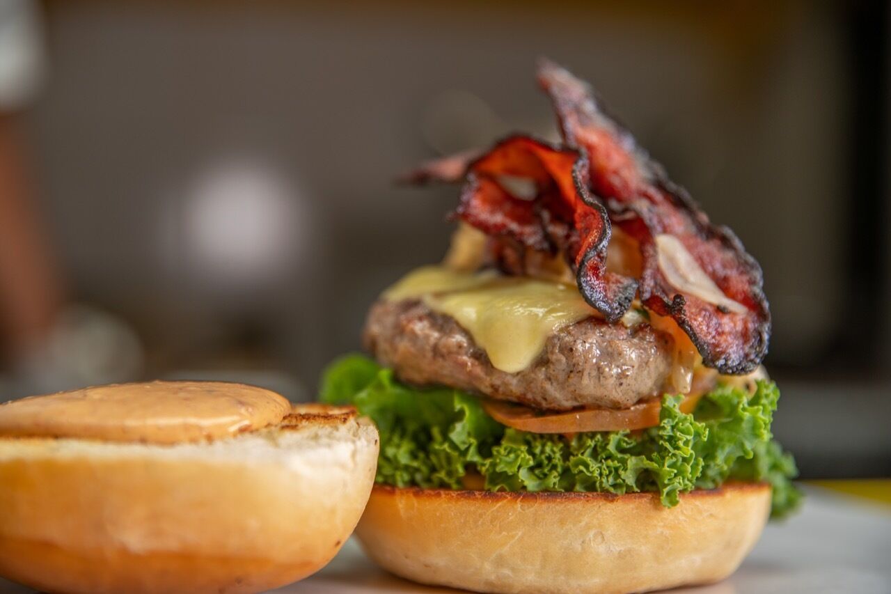 A burger with bacon and cheese on a bun, accompanied by a grilled patty and lettuce.