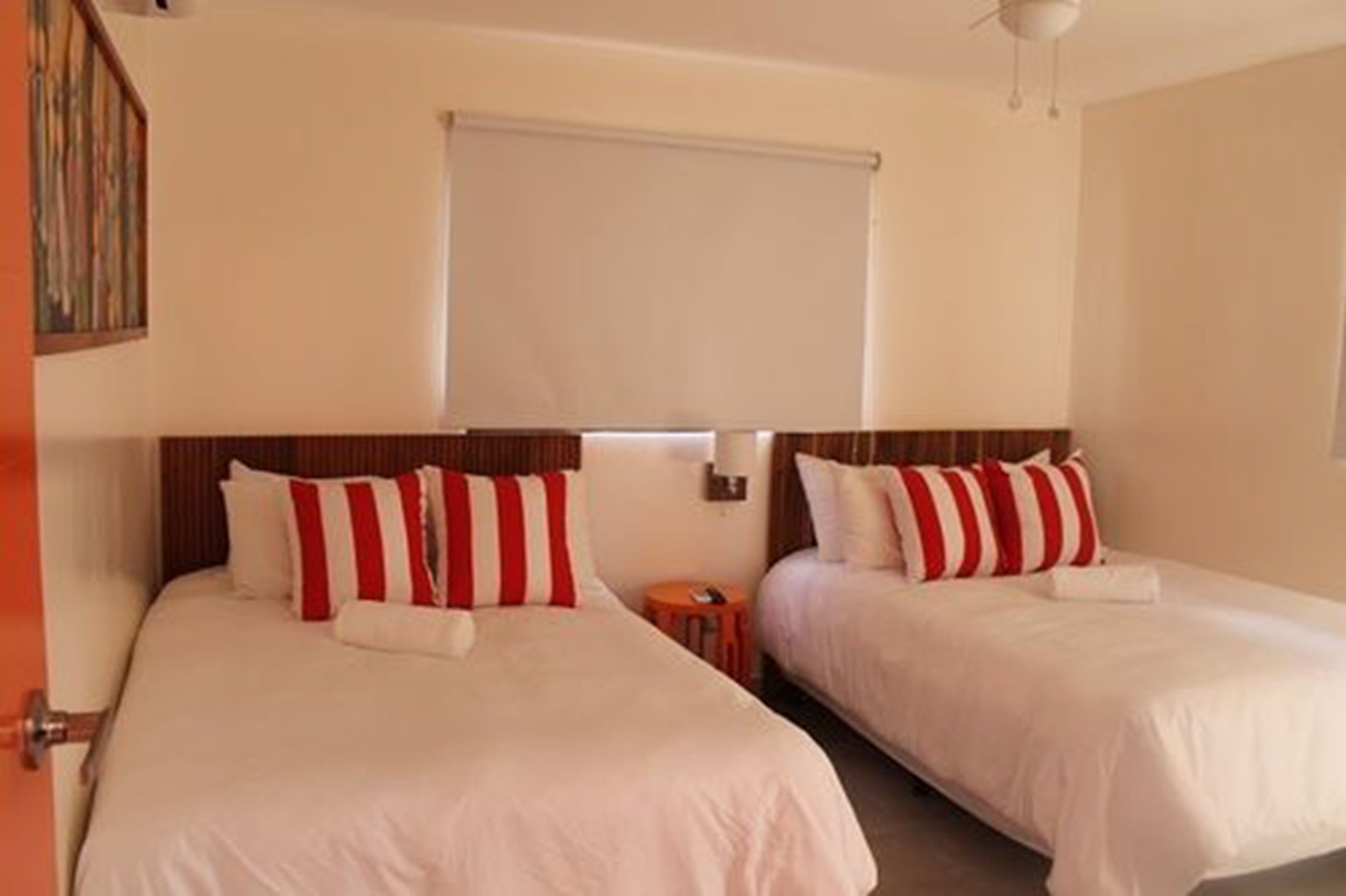 A hotel room with two beds, each with white bedding and red and white striped pillows.