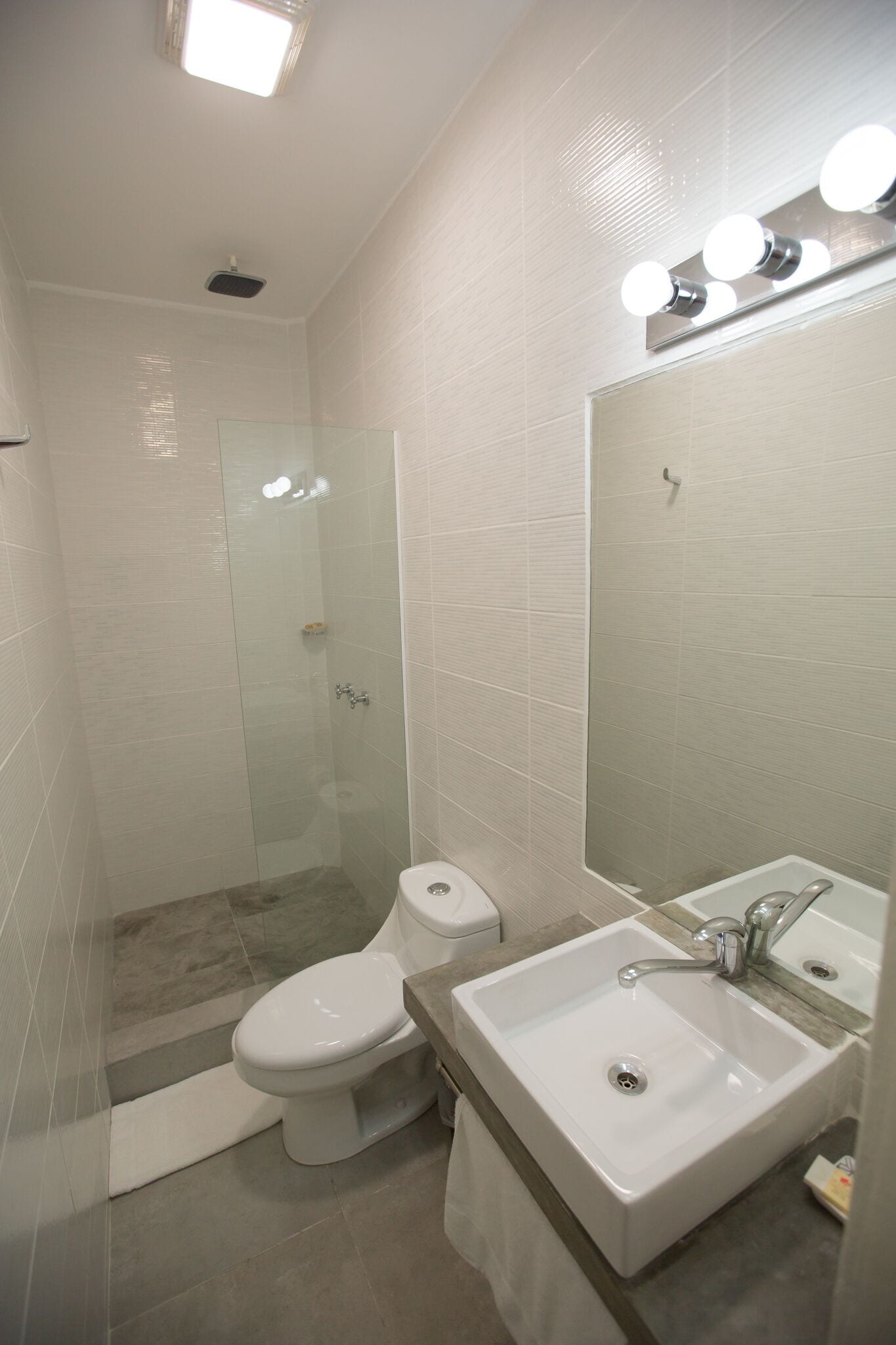 A modern bathroom with a glass shower enclosure, a toilet, a sink with a mirror, and a light fixture above the mirror.