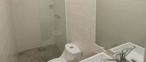 A modern bathroom with a glass shower enclosure, a toilet, a sink with a mirror, and a light fixture above the mirror.