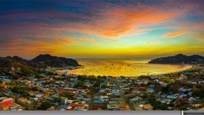 A coastal town with a beach, houses, and a hilly landscape.