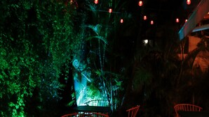 An outdoor seating area with red chairs and tables, surrounded by greenery and string lights.