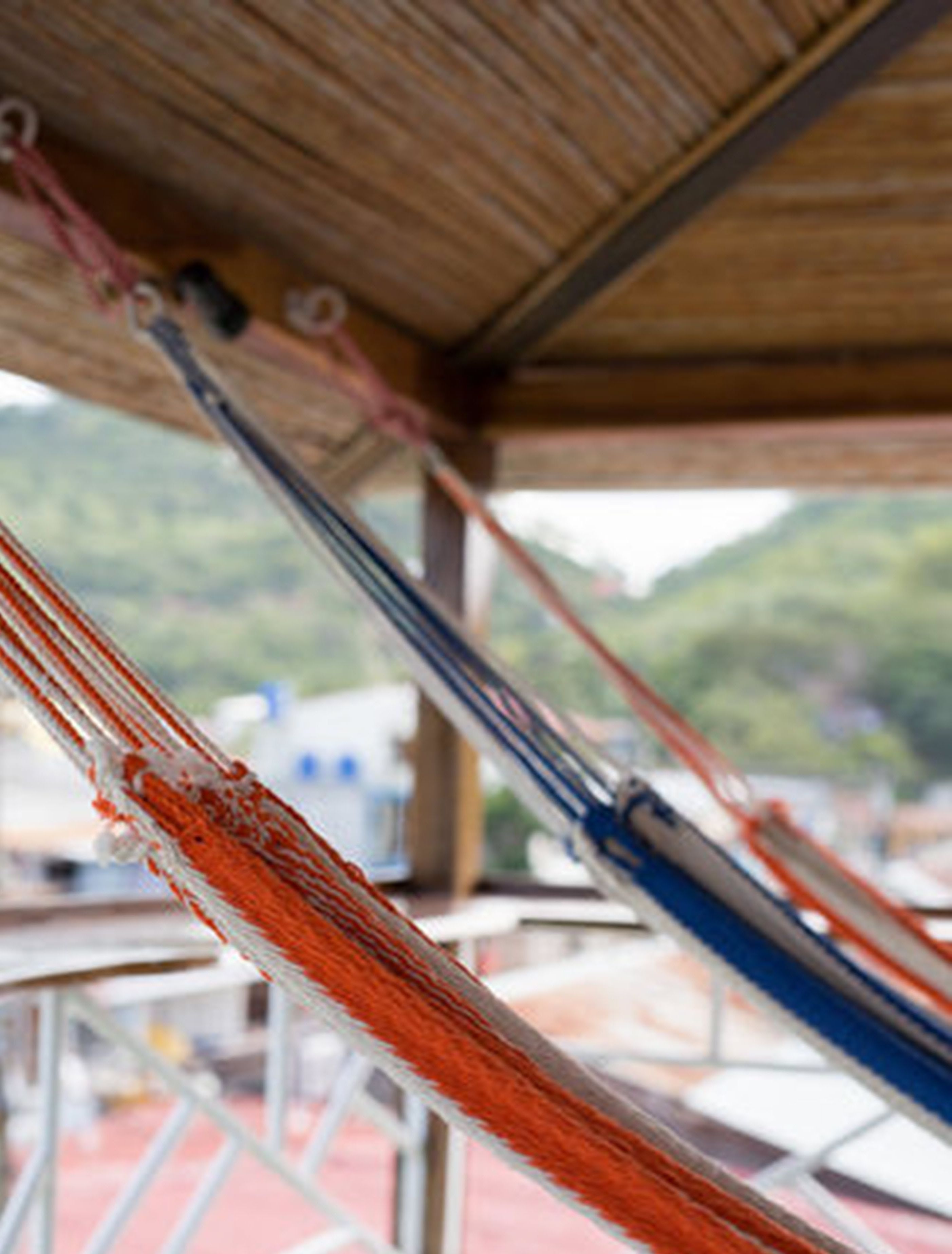 Una hamaca bajo una estructura de madera con vistas a follaje y edificios al fondo.