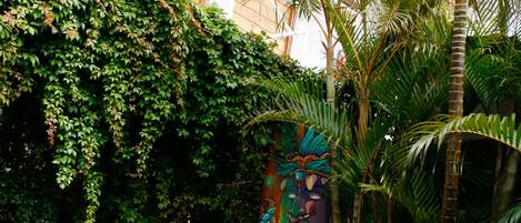 An outdoor seating area with red and blue chairs and tables, surrounded by lush greenery and a decorative wall.