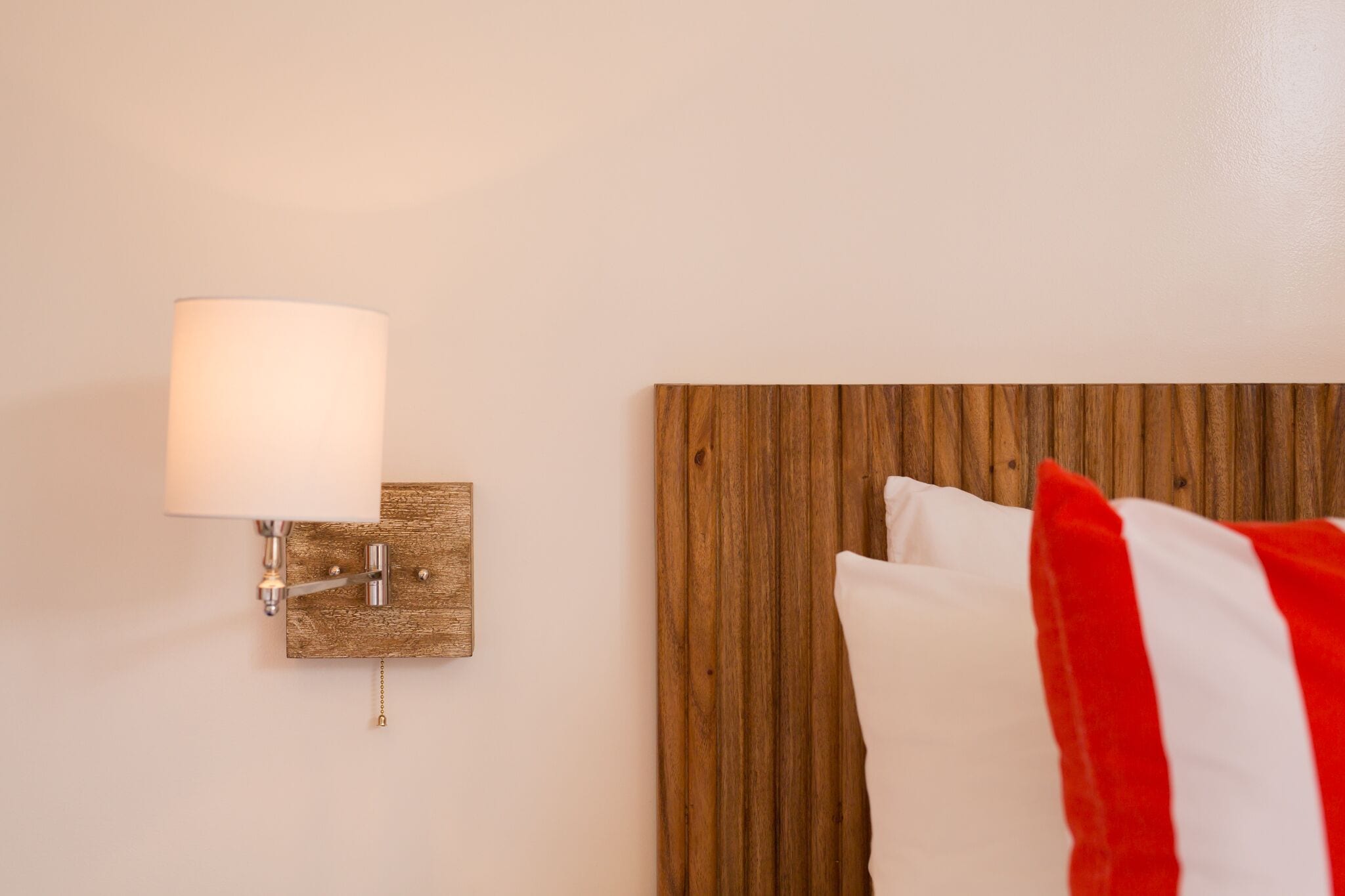 A hotel room with a wooden headboard, a wall-mounted lamp, and a bed with white and red pillows.