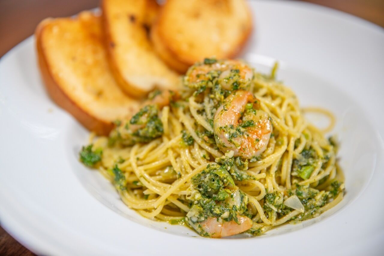 Un plato de espagueti con camarones y salsa verde, acompañado de rebanadas de pan tostado.