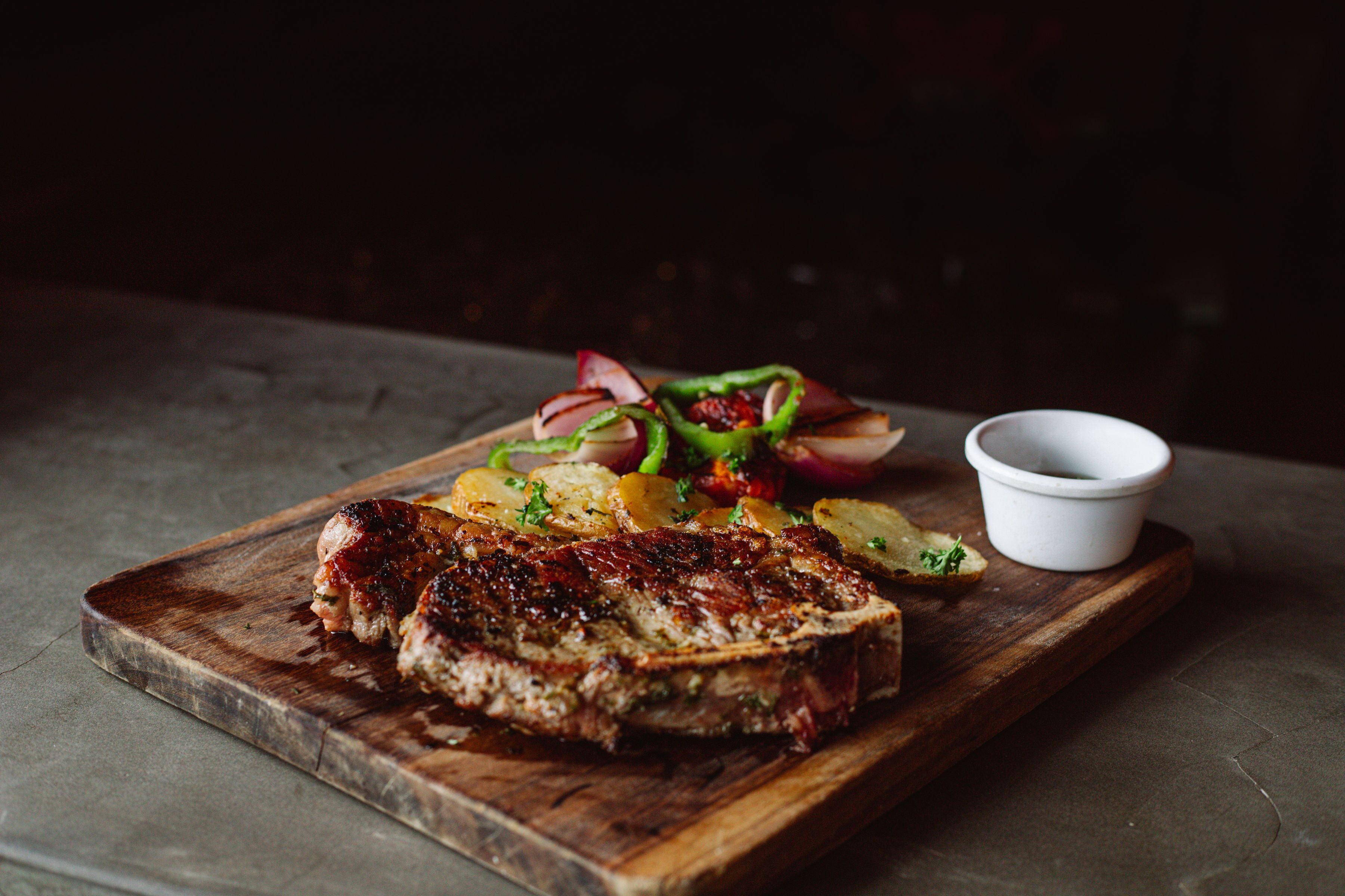 Un bife con papas asadas y una ensalada sobre una tabla de madera.