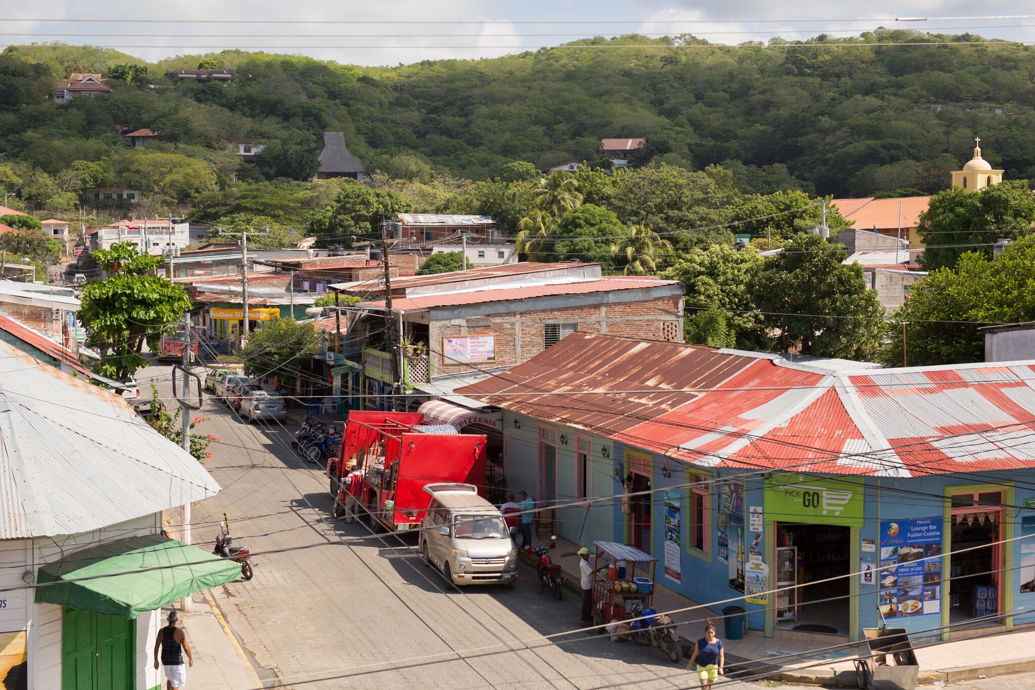 Vista da rua de uma cidade com edifícios, uma igreja e um caminhão vermelho estacionado no acostamento.