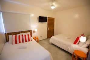 Una habitación de hotel con dos camas, un televisor, una puerta de madera y una mesita.