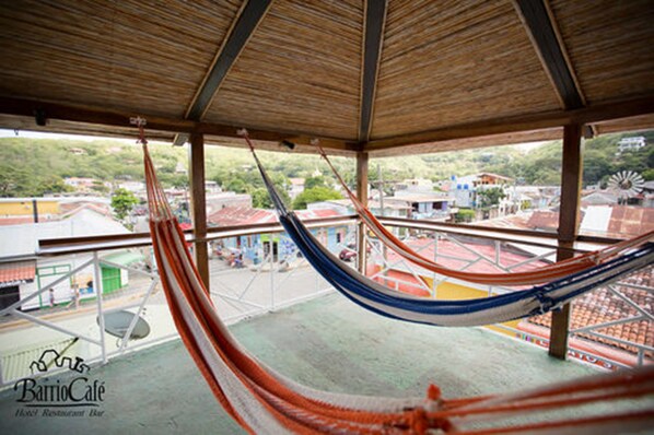 A hammock in a covered outdoor area with a view of buildings and a windmill in the background. - El Caite San Juan del Sur (San Juan del Sur)