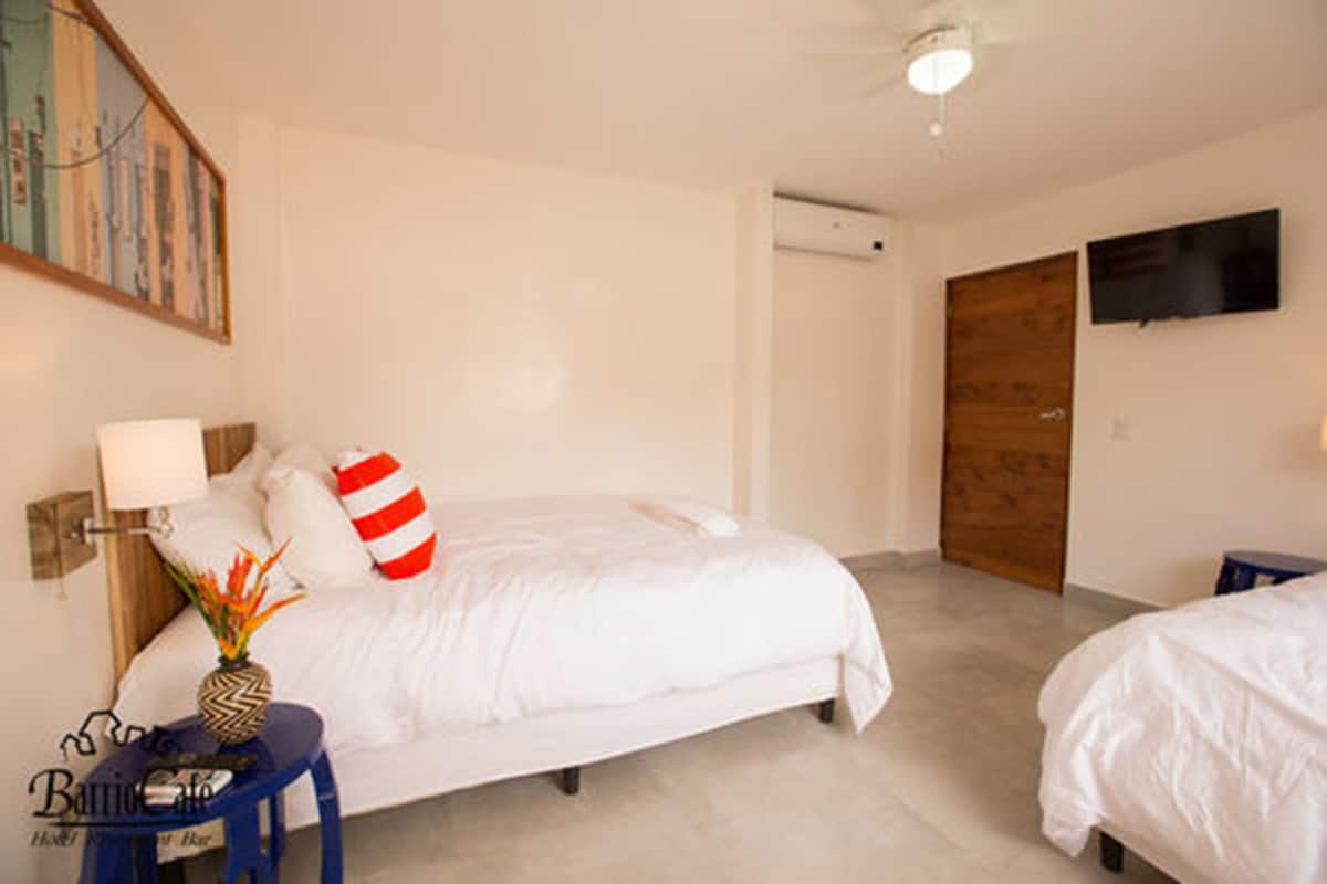 Une chambre d’hôtel avec un lit, une petite table sur laquelle se trouve un vase, un téléviseur fixé au mur et une porte en bois.