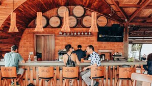 A bar with wooden chairs labeled "Flor de Cana," a brick wall, and wooden barrels on the ceiling.