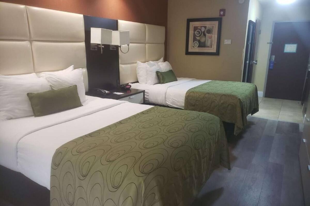 A hotel room with two beds, a nightstand, a lamp, and a framed picture on the wall.