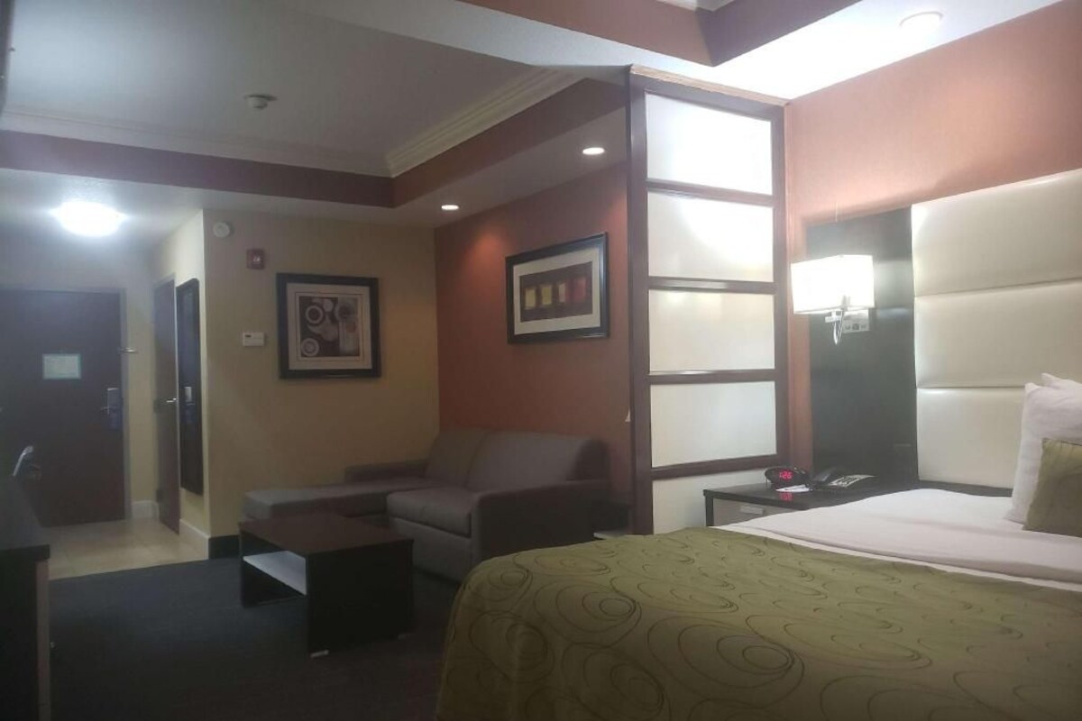 A hotel room with a bed, a chair, a desk, a nightstand, and a wall-mounted TV.