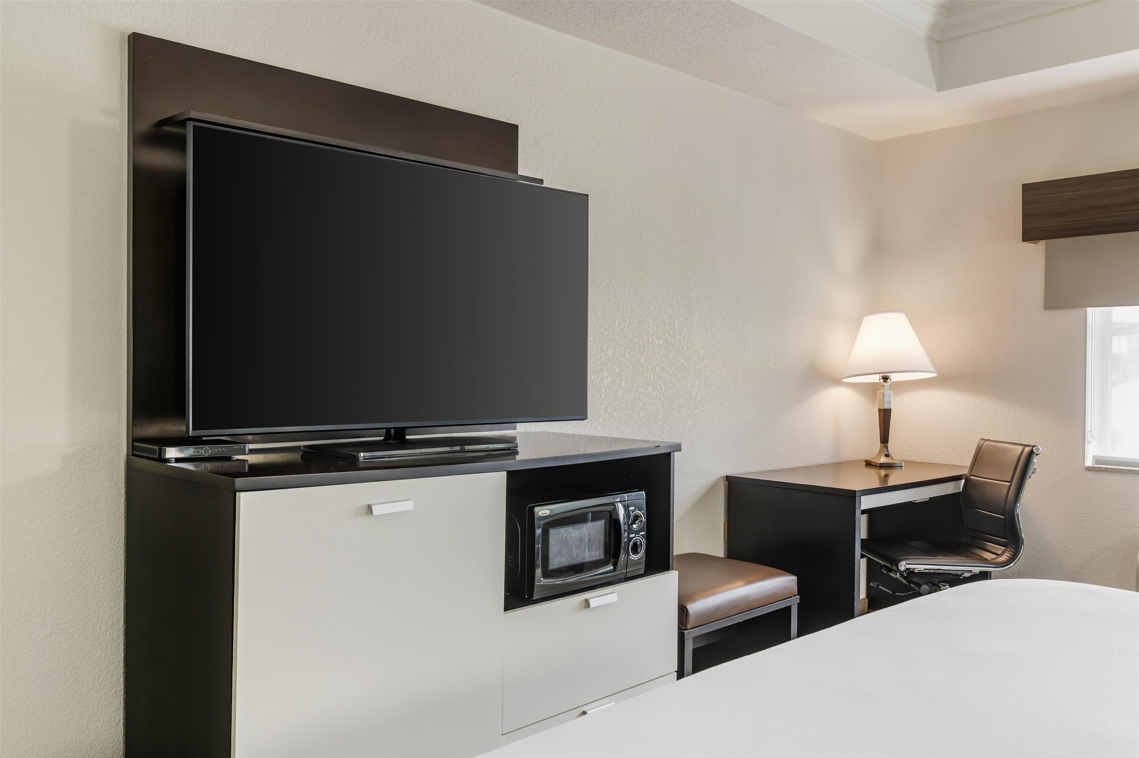 Habitación de hotel con televisor de pantalla plana, microondas, escritorio con silla y mesita de noche.