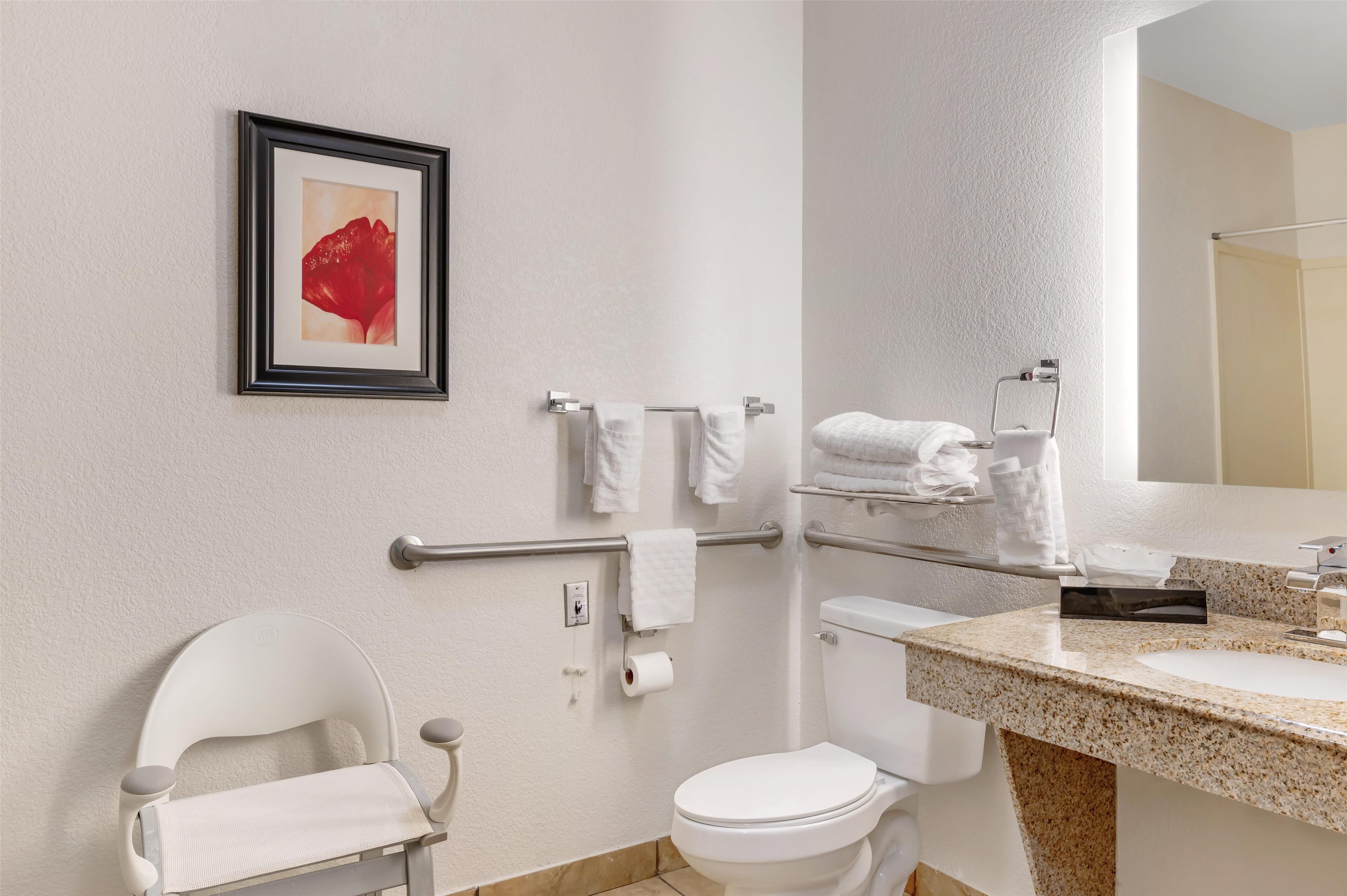 A modern bathroom with a white toilet, a white chair, a framed picture on the wall, and a sink with a mirror.