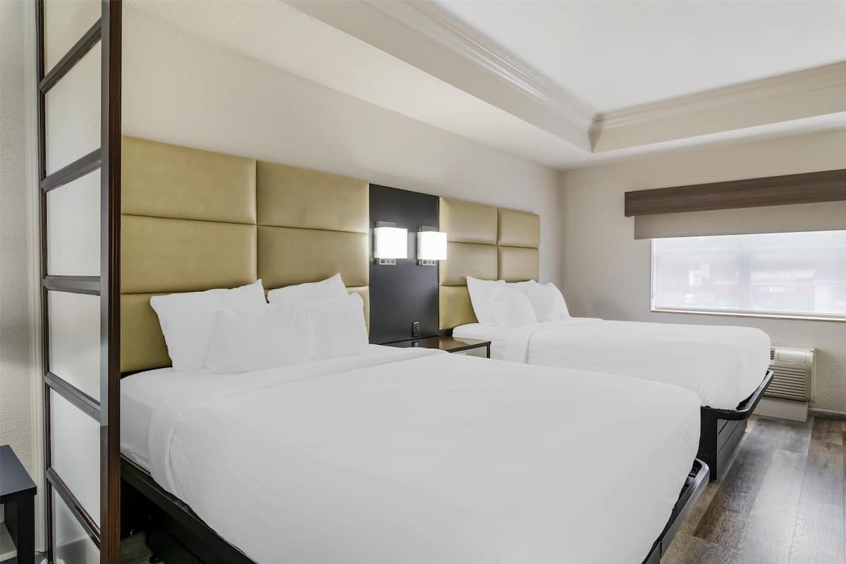 Habitación de hotel con dos camas, un ventanal grande y televisión incorporada.