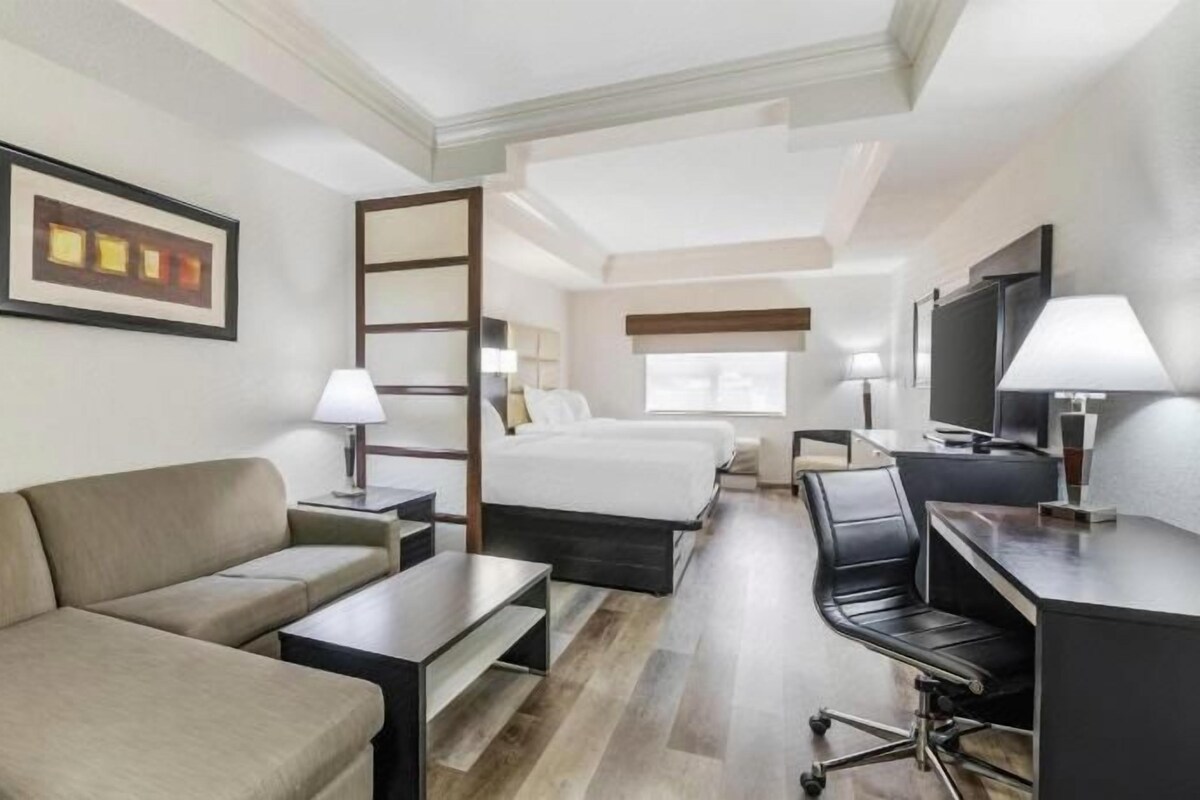 A hotel room with a bed, a sofa, a desk, a chair, and a TV.